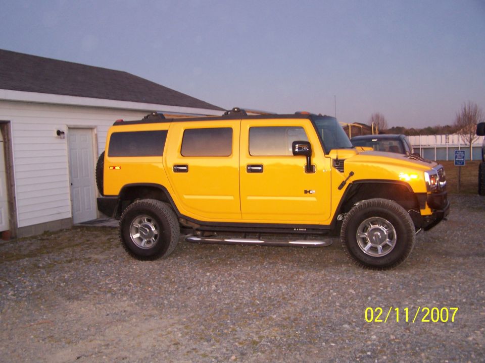 Yellow Hummer H2 SUV side view on gravel lot with chrome wheels and side steps