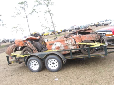 1974 Ford F-100 - A heavily damaged orange vehicle is transported on a trailer, with other vehicles visible in the background.