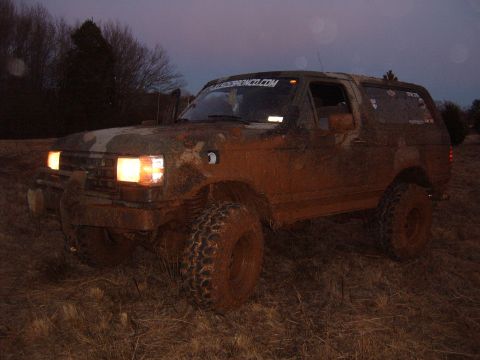 1988 Ford Bronco - This 1988 Ford Bronco is heavily covered in mud, seen off-road at dusk.