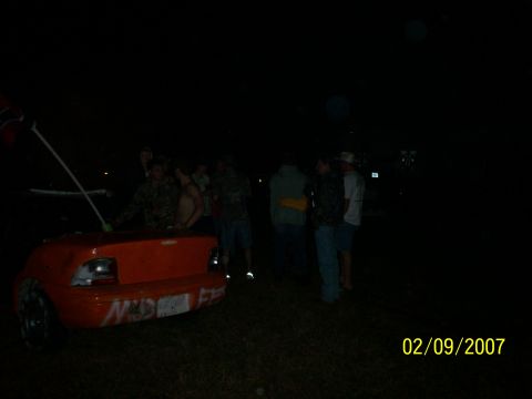 1974 Ford F-100 - An orange car trunk is visible at night, covered in graffiti, with a group of people standing nearby.