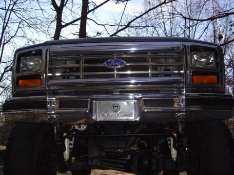 1986 Ford Bronco - Low head-on shot of a lifted 1980s Ford Bronco/F-Series front end, showing the chrome egg-crate grille with blue Ford oval, rectangular hea…
