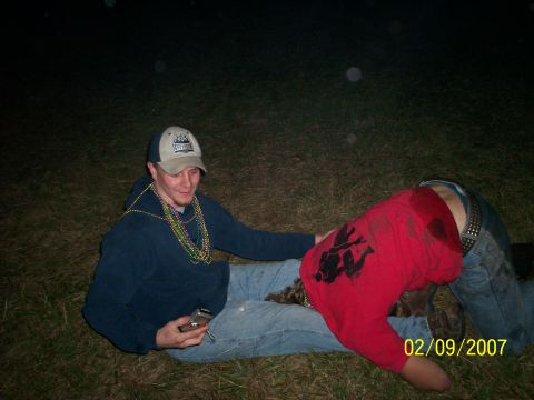 1974 Ford F-100 - Nighttime campground snapshot of two people on the grass, one seated in a ball cap and Mardi Gras beads holding a flip phone, the other slu…