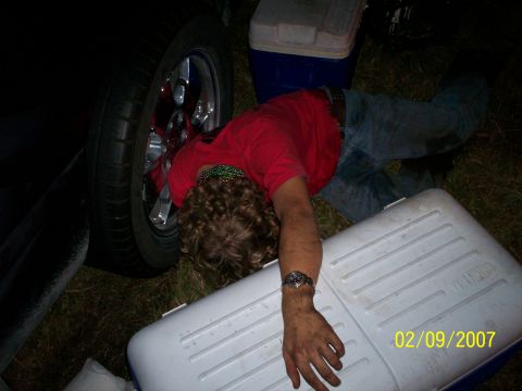 1974 Ford F-100 - Person lying down next to a vehicle wheel and coolers. Date stamp visible in the corner.