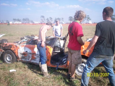 1974 Ford F-100 - A group of people examine a heavily damaged car in an open field on a sunny day.