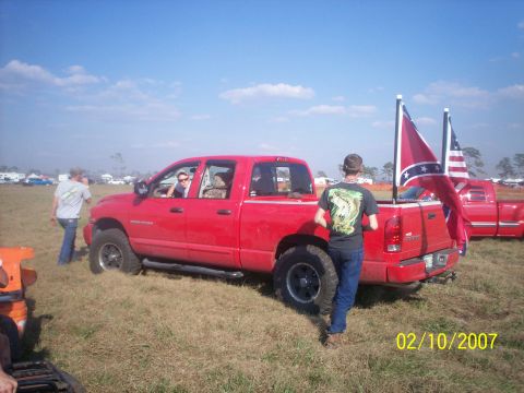 1974 Ford F-100 - A red pickup truck is parked in a grassy field with two flags, including a confederate flag, displayed in the bed.
