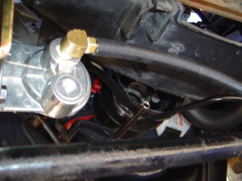 1986 Ford Bronco - Tight underhood close-up of a polished aluminum remote oil filter adapter or fuel filter housing with a brass fitting and black rubber line…