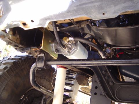1986 Ford Bronco - Underside view of a truck showing a newly installed white spin-on fuel/oil filter mounted to a gold-cadmium plated bracket bolted to the fr…
