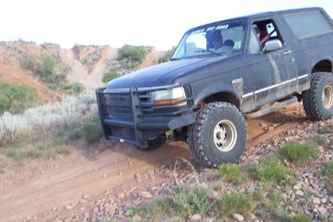 1995 Ford Bronco - A black Ford Bronco navigates a rough, off-road terrain with a prominent bull bar and lifted suspension.