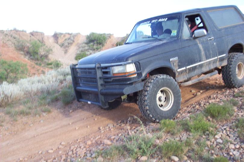 Dark Ford Bronco with brush guard and big tires on a rocky dirt off-road trail