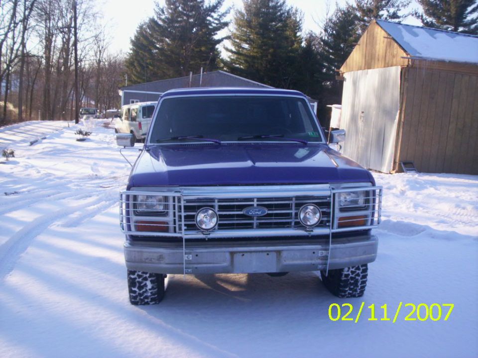 Blue 1980s Ford pickup truck with brush grille guard parked in snow