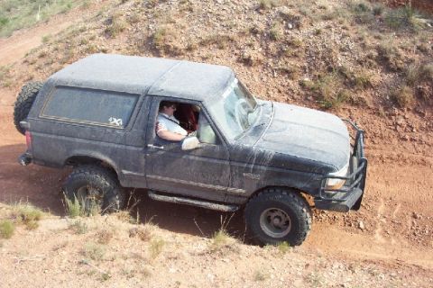 1995 Ford Bronco - A black 1995 Ford Bronco navigates a dusty, off-road trail with a spare tire mounted to the rear.