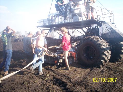 1974 Ford F-100 - Mud-splattered tube-chassis mega truck with a diamond-plate deck and roll cage full of riders, bogged down in a churned mud pit with a fire…