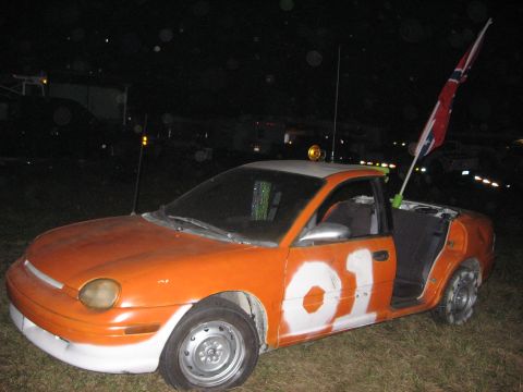 1974 Ford F-100 - This modified car, painted orange with white '01' markings, flies a confederate flag from its bed.