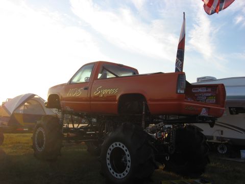 1974 Ford F-100 - A lifted orange truck with large tires and "NDS Express" lettering is parked outdoors near a tent and RV.