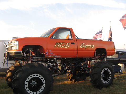 1974 Ford F-100 - Driver-side view of an orange 1990s GM regular-cab long-bed pickup built as a mud racer, lettered 'NOS Express' in gold script with sponsor…