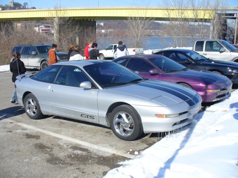1991 Ford Probe - A silver 1991 Ford Probe GTS with racing stripes is parked in a snowy lot next to other vehicles.