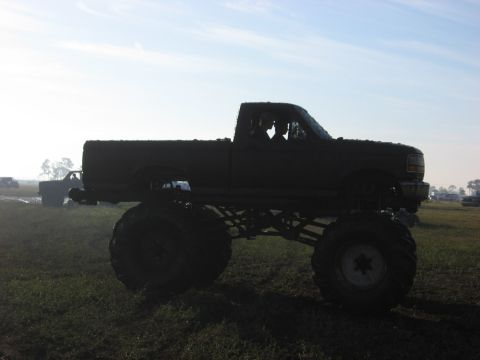 1974 Ford F-100 - A heavily modified pickup truck with oversized tires sits in a grassy field under a bright sky.