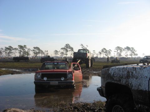 1974 Ford F-100 - Several trucks are stuck in a muddy field under a clear sky.