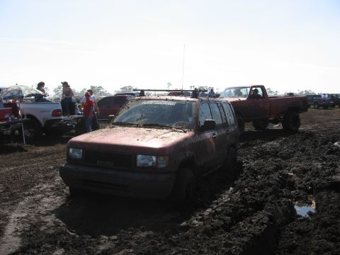 1974 Ford F-100 - Several vehicles are stuck in a mud pit during an outdoor event.