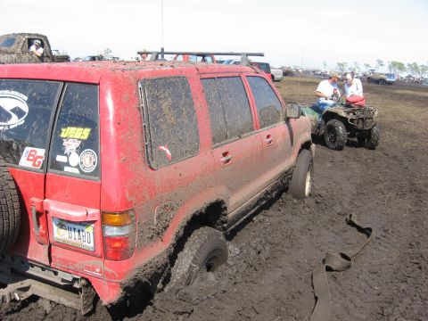 1974 Ford F-100 - A red SUV is deeply stuck in mud, with other vehicles and ATVs visible in the background.