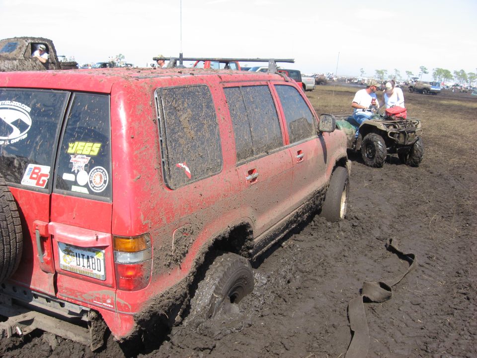 Red SUV stuck in mud with a spare tire on the back. Stickers on the rear window include 'JEGS' and 'BG'