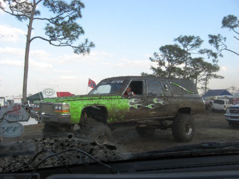 1974 Ford F-100 - Modified hearse with flame decals and lifted suspension driving through mud.