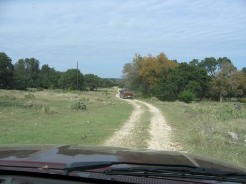 1996 Ford Bronco - Two vehicles travel on a dirt road through a rural landscape under a cloudy sky.