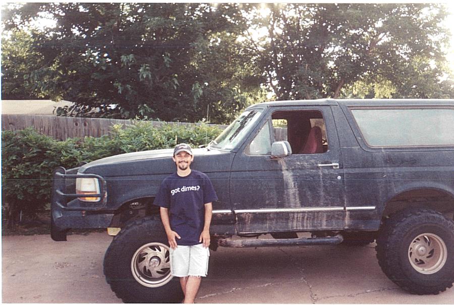 Man standing in front of a lifted dark Ford Bronco SUV with big tires and brush guard