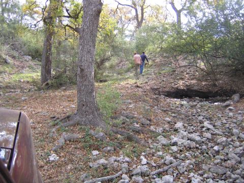 1996 Ford Bronco - A partial view of a brown vehicle is seen in a wooded, rocky area with two people walking in the distance.