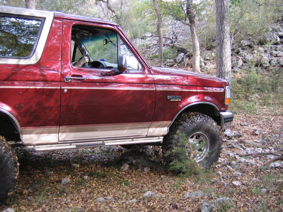 Red 1996 Ford Bronco with chrome wheels parked off-road