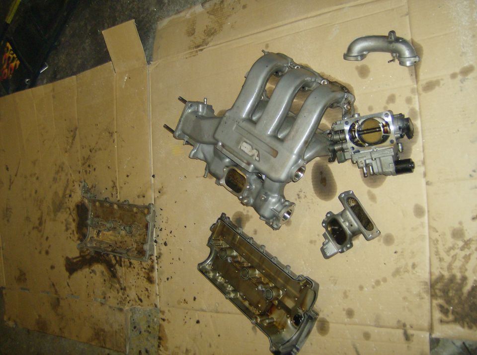 Engine intake manifold, throttle body, and valve cover disassembled on cardboard