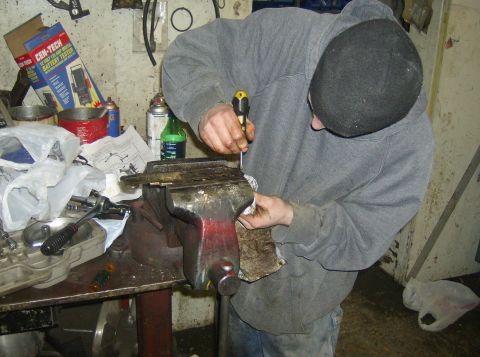 1996 Ford Probe - A person works on a metal component secured in a vise, surrounded by tools and automotive supplies in a workshop setting that appears to be…