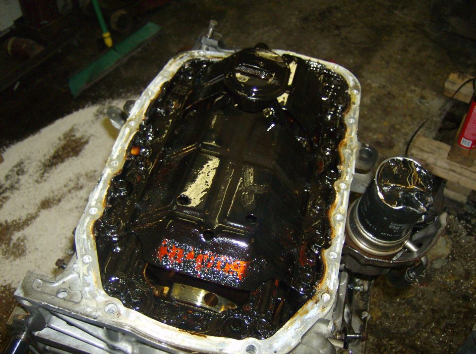 Engine oil pan filled with black sludge and a damaged oil filter