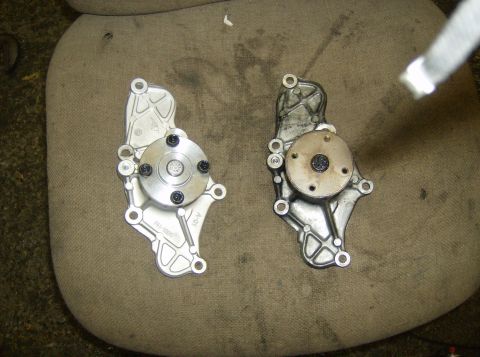 1996 Ford Probe - A comparison of a new water pump next to a used one, both resting on a textured fabric.
