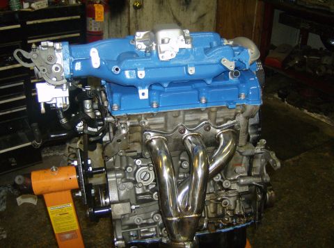 1996 Ford Probe - Engine with blue intake manifold and chrome exhaust headers, mounted on an orange engine stand in a workshop.