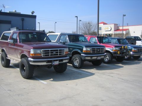1996 Ford Bronco - A row of four lifted 1992-96 Ford Broncos angled nose-out in a restaurant parking lot at a club meet: maroon with a tan top in front, then…