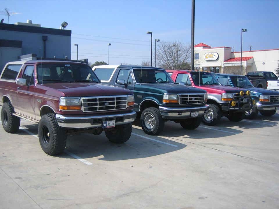 Four lifted Ford Broncos lined up in a parking lot at a club meet
