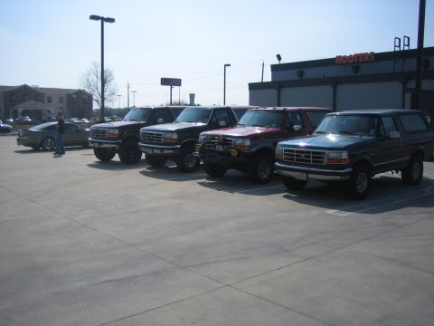 1996 Ford Bronco - A lineup of Ford Broncos and trucks are parked in a lot, with a Hooters restaurant visible in the background.