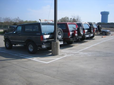 1996 Ford Bronco - Several SUVs are parked in a lot, with a dark green Ford Bronco in the foreground.