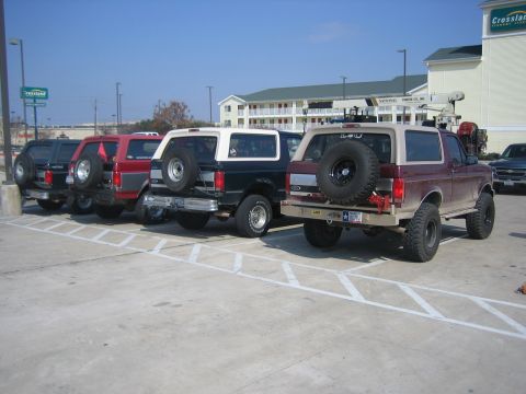1996 Ford Bronco - Four Ford Broncos, including a maroon 1996 model, are parked in a lot on a sunny day.