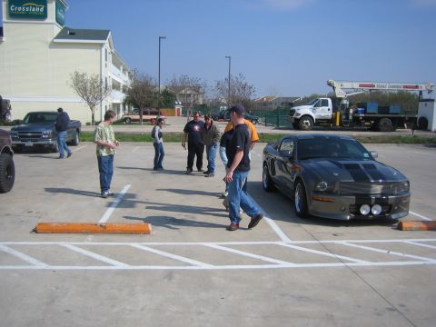 1996 Ford Bronco - Gray Ford Mustang with black racing stripes parked in a lot with several people nearby.