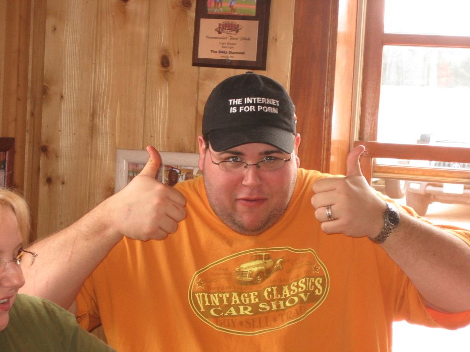 Man in orange t-shirt with vintage car graphic and cap that reads "THE INTERNET IS FOR PORN"