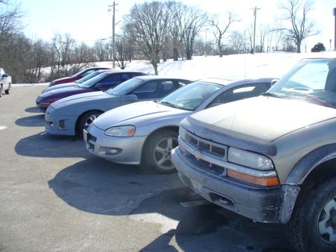1991 Ford Probe - A line of cars, including a silver sedan and a pickup truck, are parked in a lot with snow on the ground.
