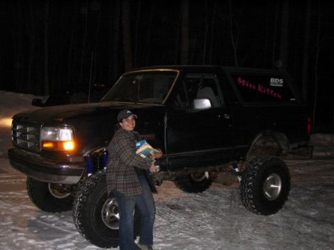 1995 Ford Bronco - A person stands next to a modified black Ford Bronco with large tires in a snowy, wooded area at night.