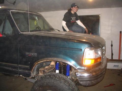 1995 Ford Bronco - A person sits on the hood of a dark green Ford Bronco, which appears to be modified with a lifted suspension.