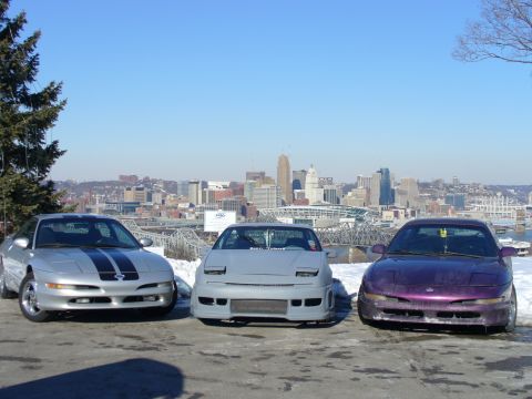 1991 Ford Probe - Three Ford Probes are parked in front of a city skyline on a clear day.