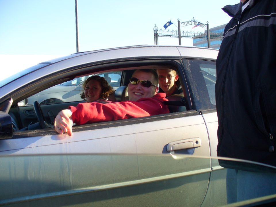 Silver car interior with three people smiling, driver's side door open