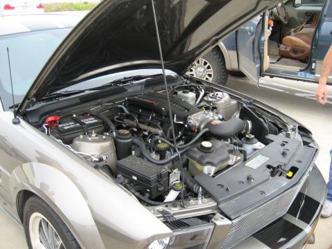 1986 Ford Bronco - The engine compartment of a car is shown with the hood raised, and a second vehicle is visible in the background.