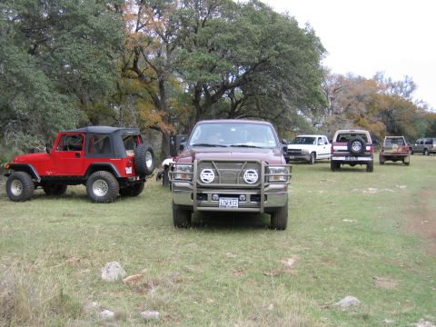 1996 Ford Bronco - Several trucks and a Jeep are parked in a grassy, wooded area.