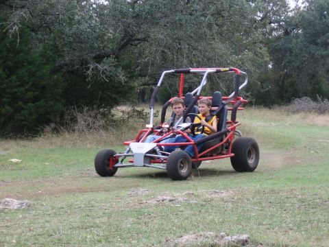 1996 Ford Bronco - Two boys ride in a red dune buggy through a grassy, wooded area.